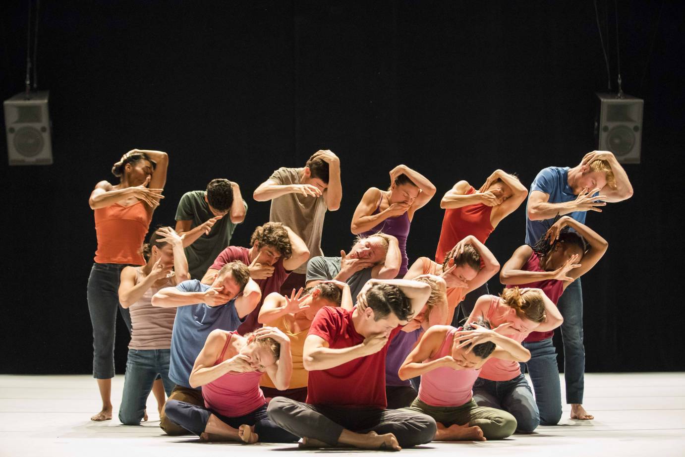 Sixteen dancers form a pyramid as they clutch their heads and hold a hand over their mouths